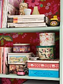 Zeitschriften und Vintage Blechdosen im Regal mit roter Blumentapete an Rückwand