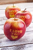 Three red apples carved with hearts and the words 'I love you'