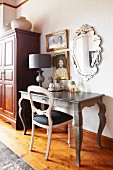 Rococo desk, table lamp and chair below pictures and mirror on wall