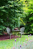 Romantischer Gartenplatz mit Tisch und zwei verzierten Eisen-Gartenstühlen im Antikstil
