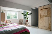 DIY sliding door made from various wooden panels and houseplant on plain wooden table in bedroom