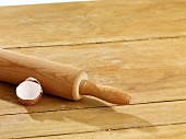 A rolling pin and an eggshell on a wooden surface