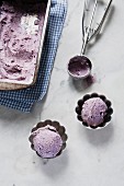 Blueberry ice cream in a loaf tin and small bowls with an ice cream scoop