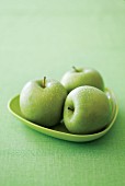 Three Granny Smith apples on a green plate on a green surface