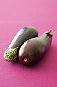 Two aubergines on a pink surface