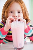 A little girl blowing bubbles into her milkshake