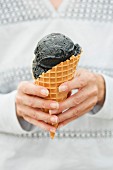 A hand holding black ice cream in a conr