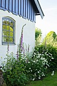 Sommerliches Blumenbeet vor Landhaus mit blauer Holzverschalung