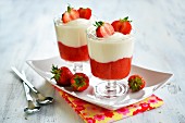 Desserts made with strawberry mousse and yoghurt in glasses on a tray garnished with fresh fruit