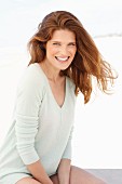 A young brunette woman on a beach wearing a pastel green jumper