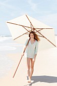 Junge brünette Frau in dünnem Pulli hält grossen Sonnenschirm