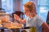 A blonde girl tasting food while cooking