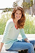 A young brunette woman on a beach wearing jeans and a pastel green jumper