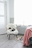 Rattanstuhl mit weißem Schaffell und Katze neben rosa Wolldecke und Zeitschriften