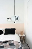 Black pillows on white bed linen below shelf on wall with pink painted dado