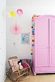 Romantisches Mädchenzimmer mit pinkfarbenem Holzschrank und Korbschaukelstuhl