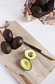 Whole avocados and a halved avocado on a wooden board (seen from above)