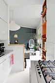 Gasherd und weiße Küchenzeile in offenem Wohnbereiche, im Hintergrund Hängestuhl vor grauer Wand
