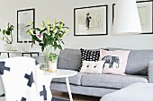 Scatter cushions on pale grey couch and vase of lilies on round table