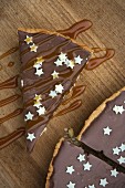 Tarte au chocolat decorated with small white stars and caramel sauce on a wooden board