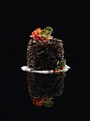 Black Food: Schwarzer Reis-Timbal mit Bacon, Schaum und Blatt auf schwarzem Untergrund mit Reflexion
