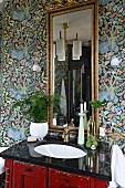 Houseplant on vintage washstand with black polished top below gilt-framed mirror