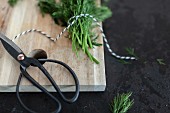 Kitchen scissors and twine with dill on a chopping board