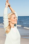 A young blonde woman on a beach wearing a pastel green jumper