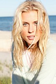 A young blonde woman on a beach wearing a pastel green jumper