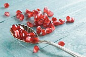 A spoon with pomegranate seeds on a wooden surface