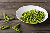 A bowl of peas and pea pods next to it