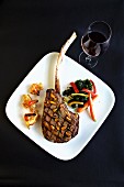 Grilled tomahawk steak with sides and a glass of red wine (seen from above)