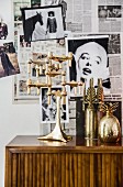 Gold candlesticks and vase in front of wall covered in black and white photos and newspaper pages