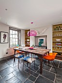 Vintage dining table, metal chairs and orange retro chairs in front of fitted shelving and lattice window