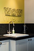 White sink in granite kitchen worksurface below decorative lettering on yellow wall