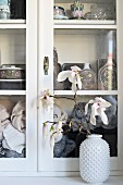 Branch of flowering magnolia in white vase with structured surface inn front of display case