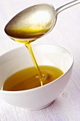Olivenöl fliesst vom Löffel in ein Schälchen
