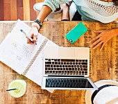 Frau arbeitet mit Laptop und Notizen im Café