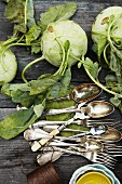 Fresh kohlrabi lying next to silver cutlery (seen from above)