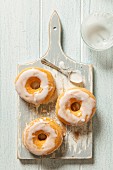 Three iced doughnuts on a grey wooden chopping board with a spoon