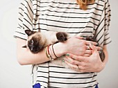 A woman holding Siamese cat