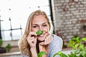 A smiling blond woman sniffing a basil leaf