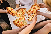 Freunde sitzen beisammen und teilen sich Pizza aus Pizzakarton