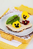 A slice of bread topped with chilli cheese, a bloodwort leaf and pansies