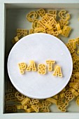 Das Wort Pasta aus Buchstabennudeln auf Teller (Aufsicht)