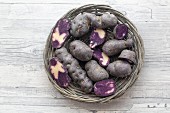 Purple potatoes, whole and halved, in a wicker basket (seen from above)