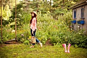A young woman wearing a hippie outfit with a watering can in a garden
