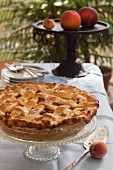 A whole peach pie with a lattice lid on a cake stand
