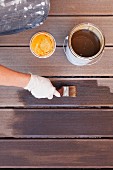Hand applying varnish to decking with paintbrush