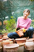 Frau zwischen Terracotta-Töpfen beim Umtopfen einer Pflanze